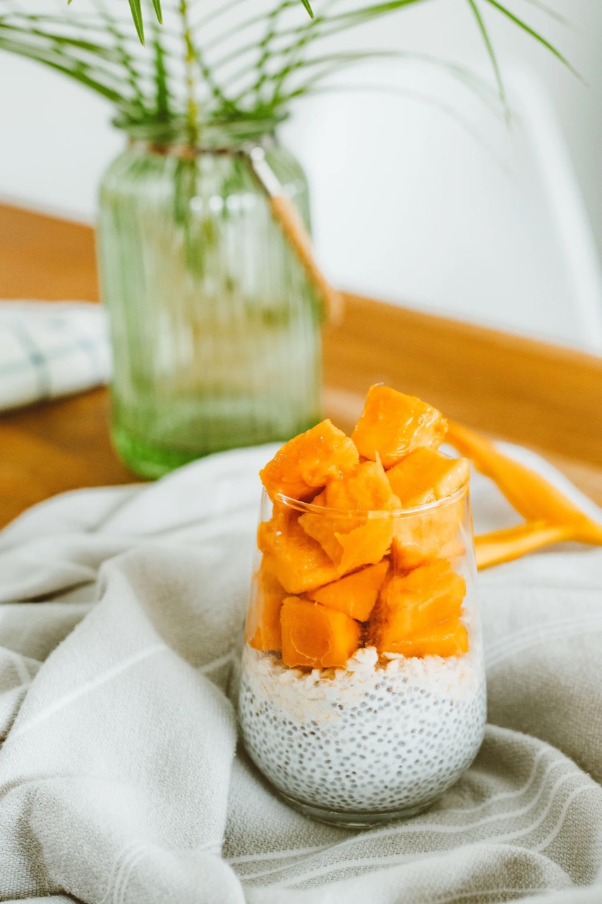 Chia pudding in a glass topped with mango cubes, set on a linen cloth beside a vase of greenery