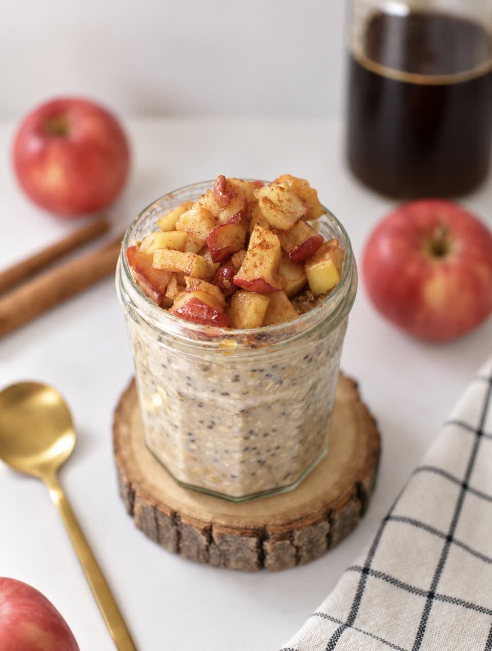 Jar of overnight oats topped with cinnamon-caramelized diced apple, surrounded by red apples